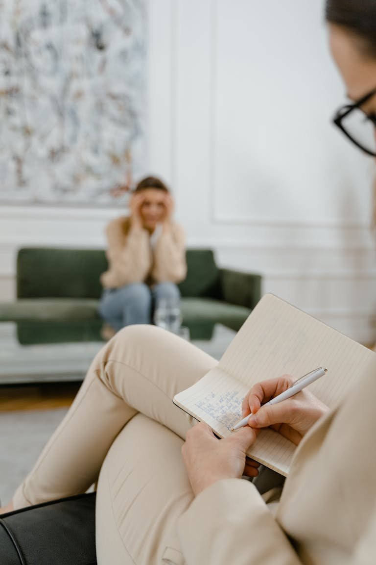 A therapist takes notes in a modern office setting during a therapy session with a patient.